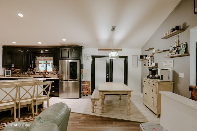 kitchen featuring lofted ceiling, sink, stainless steel refrigerator, backsplash, and light wood-type flooring