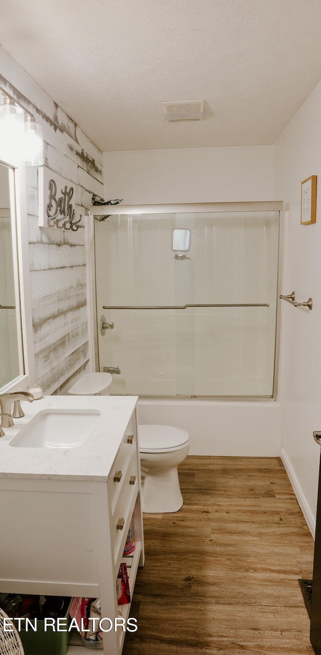 full bathroom with toilet, shower / bath combination with glass door, a textured ceiling, vanity, and hardwood / wood-style floors