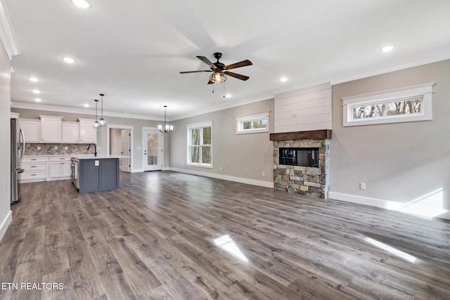 unfurnished living room with sink, ceiling fan with notable chandelier, a fireplace, wood-type flooring, and crown molding