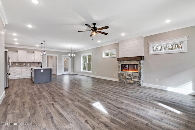 unfurnished living room featuring ceiling fan with notable chandelier, wood-type flooring, sink, ornamental molding, and a fireplace