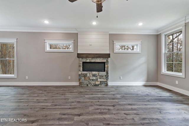 unfurnished living room with a stone fireplace, dark wood-type flooring, ceiling fan, and crown molding