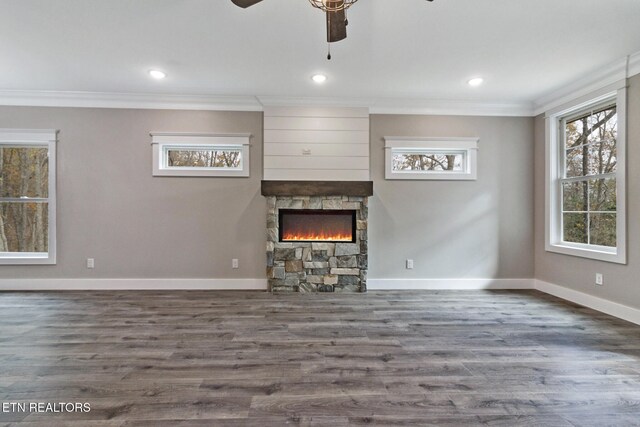 unfurnished living room with dark wood-type flooring, a stone fireplace, ceiling fan, and crown molding