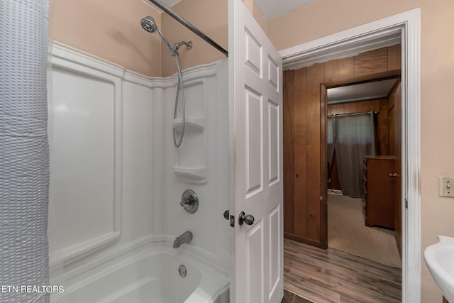 bathroom with hardwood / wood-style flooring, sink, washtub / shower combination, and wooden walls