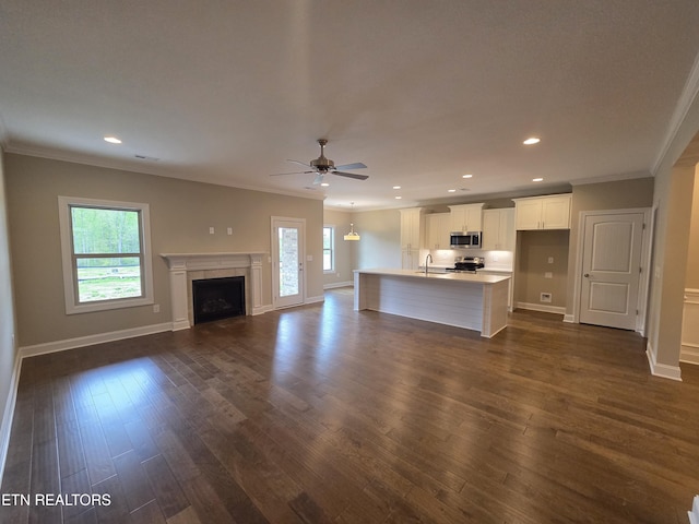 unfurnished living room with a ceiling fan, a wealth of natural light, and ornamental molding