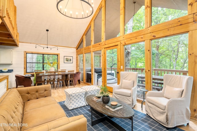 living room with hardwood / wood-style floors, a notable chandelier, high vaulted ceiling, and wooden walls