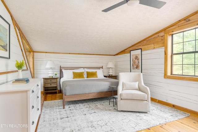 bedroom featuring wooden walls, light hardwood / wood-style floors, ceiling fan, and lofted ceiling