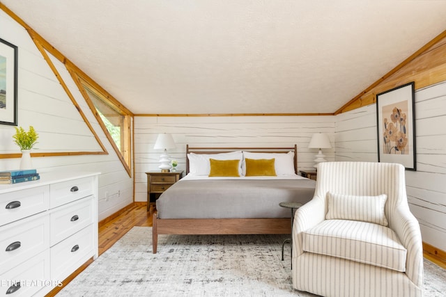 bedroom with a textured ceiling, light hardwood / wood-style flooring, wooden walls, and vaulted ceiling