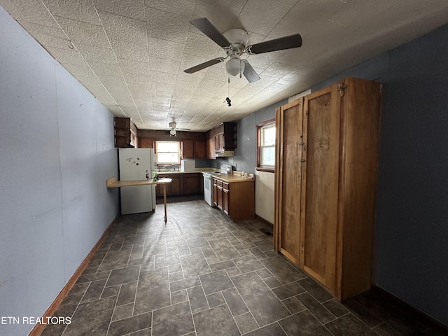 kitchen featuring white range with electric stovetop, baseboards, stone finish floor, brown cabinets, and light countertops