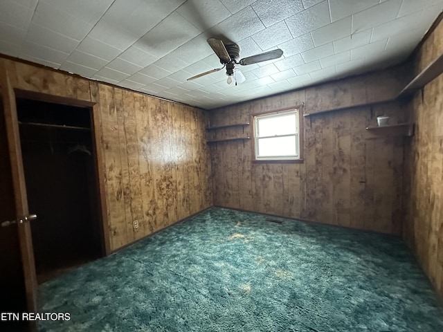 interior space with ceiling fan, wooden walls, and dark carpet