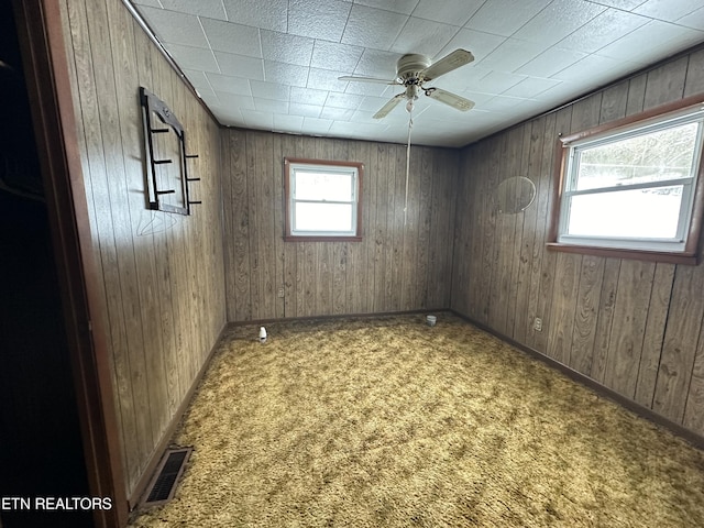 carpeted spare room with wooden walls, visible vents, and a ceiling fan