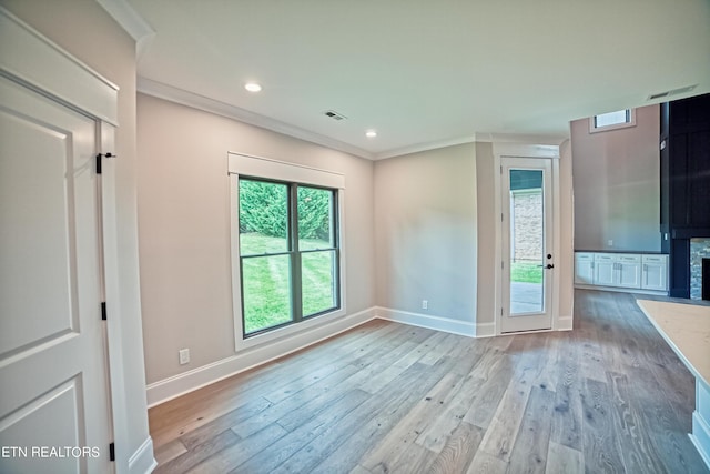 spare room featuring a stone fireplace, light hardwood / wood-style flooring, and ornamental molding