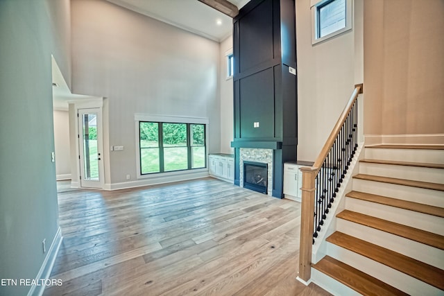 unfurnished living room with a stone fireplace, a towering ceiling, and light hardwood / wood-style flooring