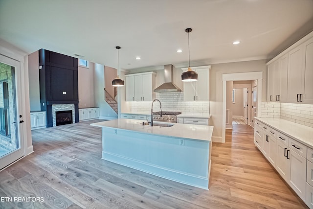 kitchen featuring white cabinetry, sink, wall chimney exhaust hood, hanging light fixtures, and a center island with sink