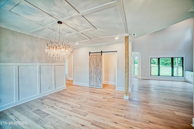 empty room with a barn door, an inviting chandelier, light wood-type flooring, and coffered ceiling