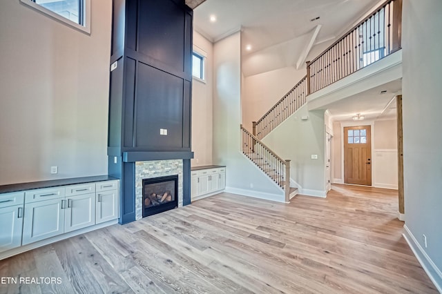 unfurnished living room with a stone fireplace, light hardwood / wood-style floors, a high ceiling, and ornamental molding