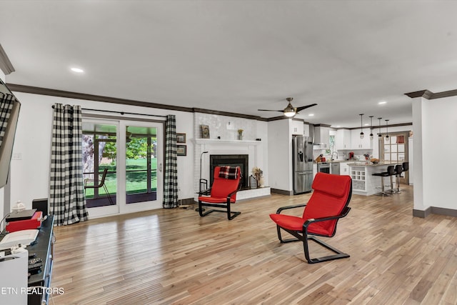 living room with a brick fireplace, ornamental molding, and light hardwood / wood-style flooring