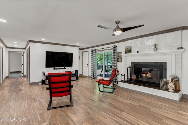 living room featuring hardwood / wood-style floors, ceiling fan, ornamental molding, and a brick fireplace