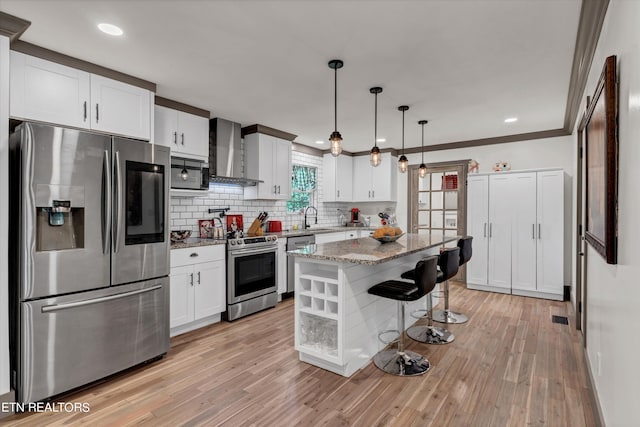 kitchen with light stone countertops, appliances with stainless steel finishes, wall chimney exhaust hood, pendant lighting, and a kitchen island