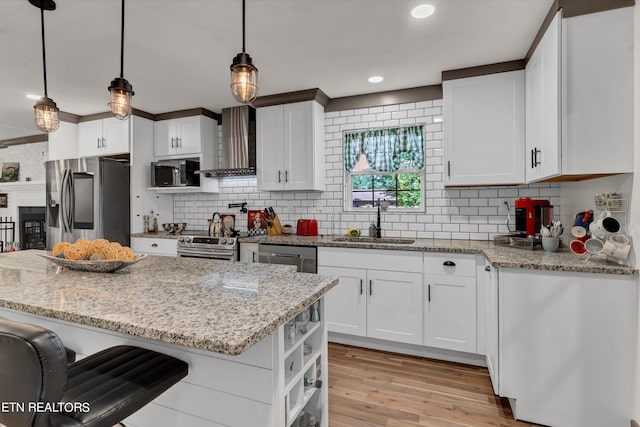 kitchen featuring white cabinets, sink, wall chimney exhaust hood, decorative light fixtures, and stainless steel appliances