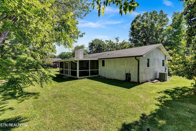 rear view of property with a yard, central air condition unit, and a sunroom