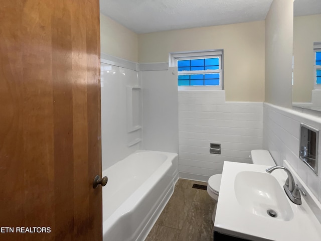 bathroom with tile patterned flooring, a textured ceiling, toilet, vanity, and tile walls