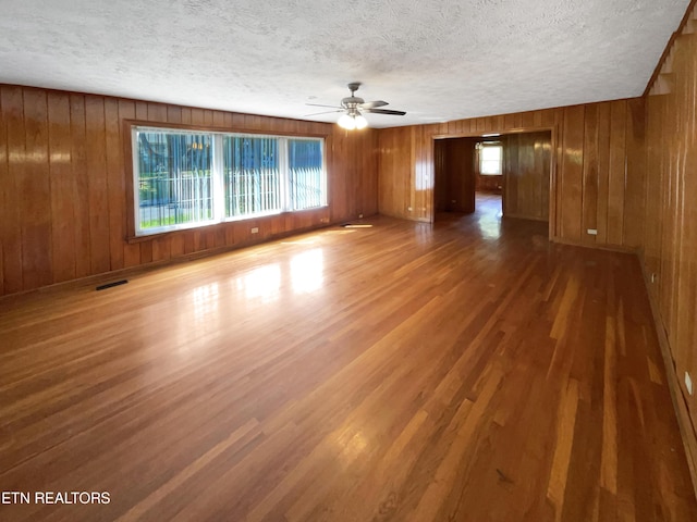 unfurnished room featuring a textured ceiling, ceiling fan, dark wood-type flooring, and wooden walls