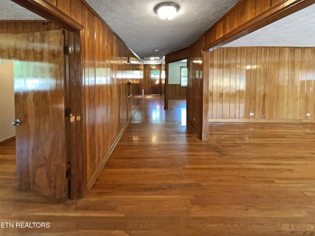 hallway featuring wood-type flooring, a textured ceiling, and wooden walls