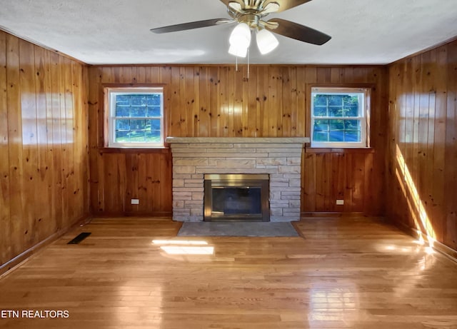 unfurnished living room featuring a stone fireplace, wood walls, and light wood-type flooring