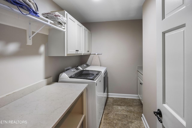 washroom with stone finish floor, cabinet space, baseboards, and washer and clothes dryer