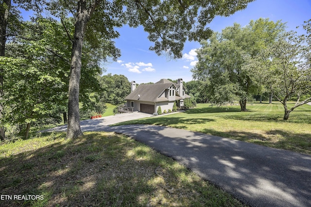 view of home's exterior with stucco siding, a chimney, a garage, a yard, and driveway