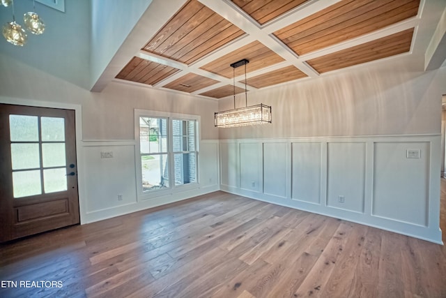 unfurnished dining area featuring hardwood / wood-style floors, coffered ceiling, and a decorative wall