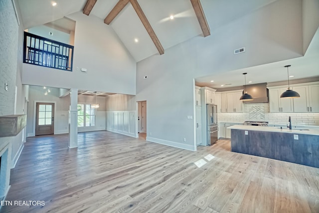 kitchen featuring light wood-style flooring, open floor plan, light countertops, beam ceiling, and wall chimney exhaust hood