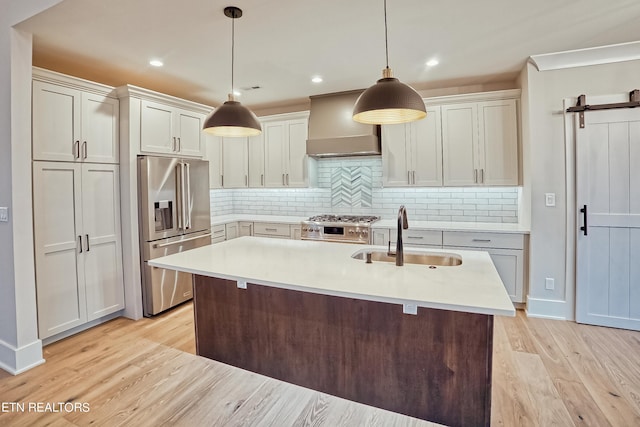 kitchen with premium appliances, light countertops, light wood-style floors, a sink, and wall chimney exhaust hood