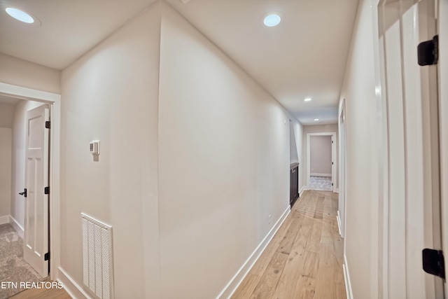 corridor featuring light wood-type flooring, baseboards, visible vents, and recessed lighting