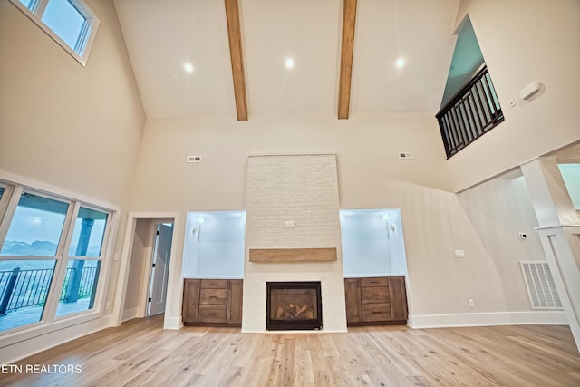 unfurnished living room with light wood finished floors, a fireplace, visible vents, and high vaulted ceiling