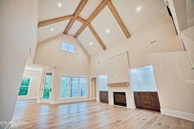 unfurnished living room featuring light wood-type flooring, plenty of natural light, visible vents, and beamed ceiling