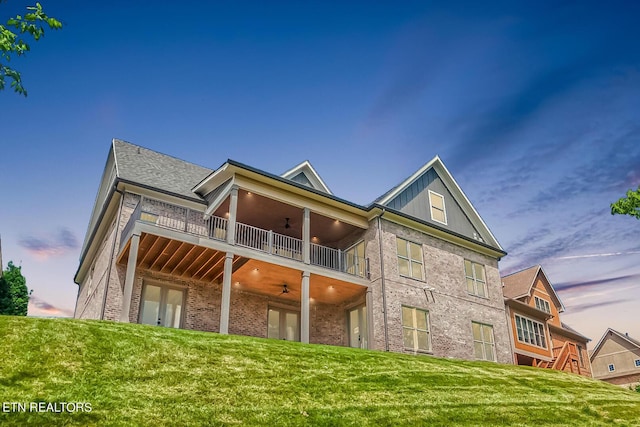 back of property with ceiling fan, a balcony, brick siding, french doors, and board and batten siding