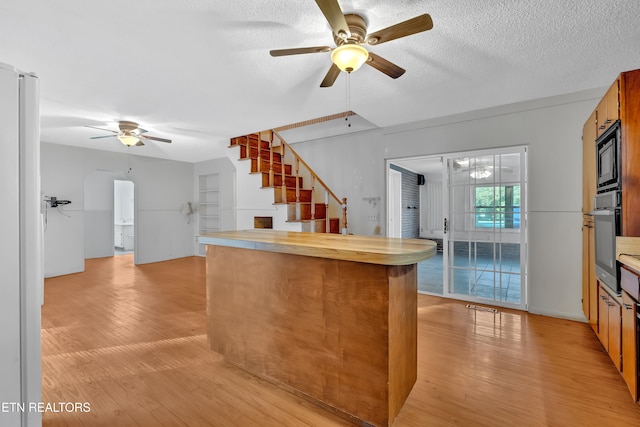 kitchen featuring oven, ceiling fan, a textured ceiling, built in microwave, and light hardwood / wood-style floors