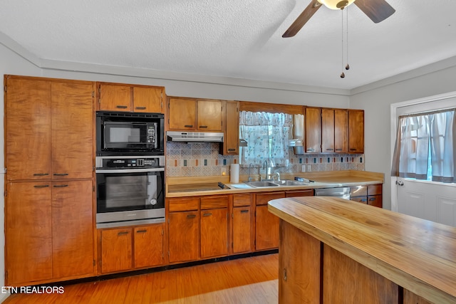 kitchen with decorative backsplash, sink, black appliances, light wood-type flooring, and ceiling fan