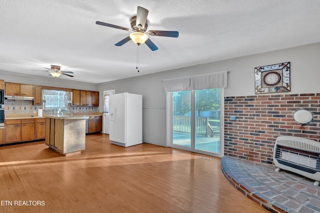 kitchen featuring decorative backsplash, white fridge with ice dispenser, a center island, heating unit, and light wood-type flooring