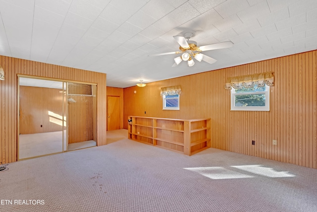 spare room featuring wooden walls, carpet floors, and ceiling fan