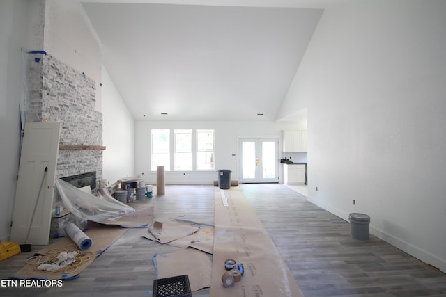 unfurnished living room featuring high vaulted ceiling, french doors, a brick fireplace, and hardwood / wood-style floors