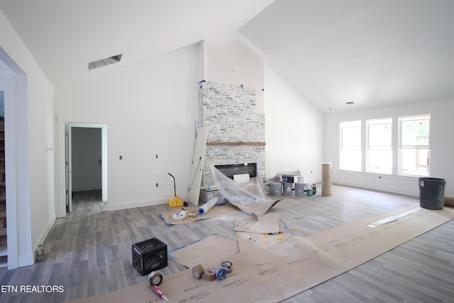 unfurnished living room with high vaulted ceiling, wood-type flooring, and a stone fireplace