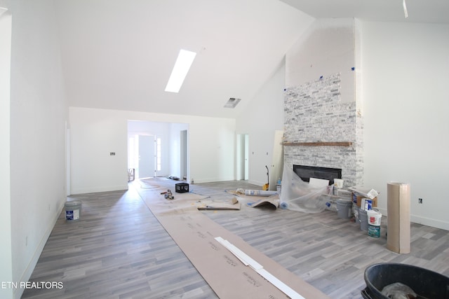 living room featuring light hardwood / wood-style floors, high vaulted ceiling, a skylight, and a stone fireplace