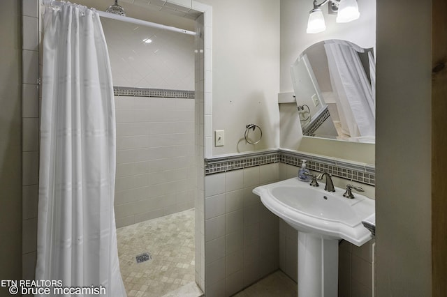 bathroom featuring curtained shower, tile walls, and sink