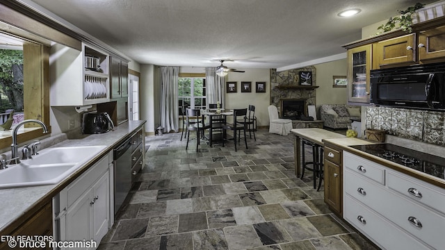 kitchen featuring sink, white cabinets, a stone fireplace, and black appliances