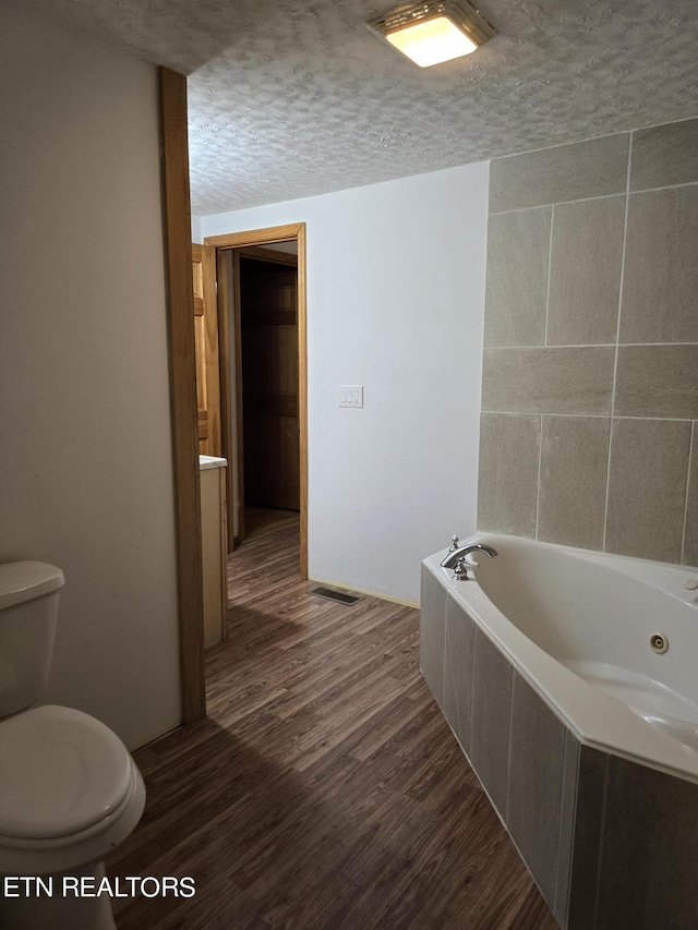 bathroom featuring a textured ceiling, hardwood / wood-style flooring, toilet, and tiled tub