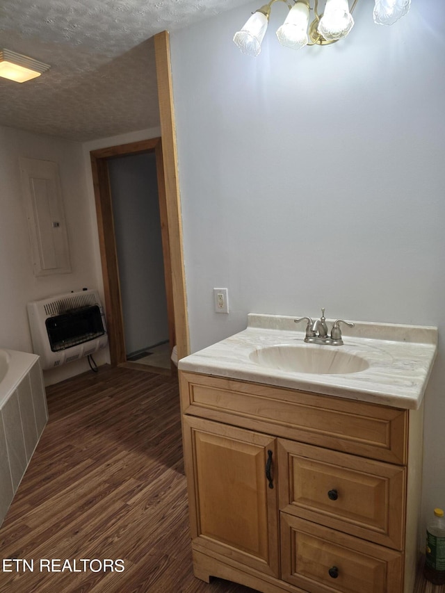 bathroom with a bath, heating unit, wood-type flooring, a textured ceiling, and vanity