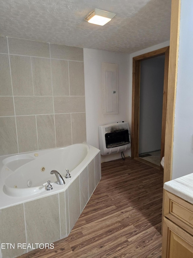 bathroom with electric panel, heating unit, hardwood / wood-style flooring, and a relaxing tiled tub