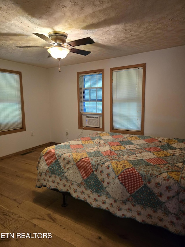 bedroom with ceiling fan, cooling unit, light hardwood / wood-style floors, and a textured ceiling